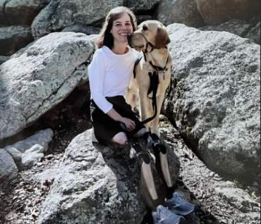 Susan, an OPRA™ Implant System patient, seated on rocks outdoors with her dog.